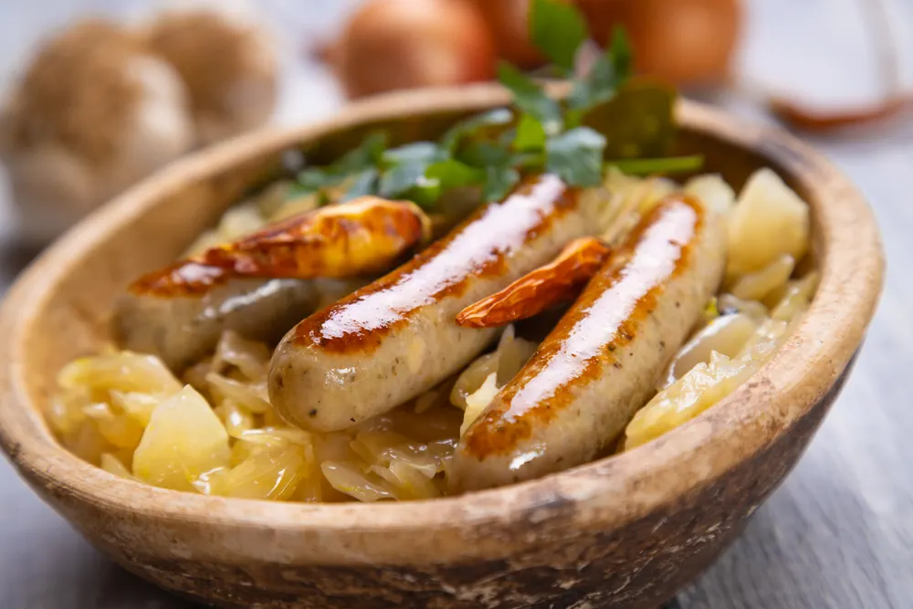 3 grilled bratwurst in a bowl filled with sauerkraut, two of the best German foods to try