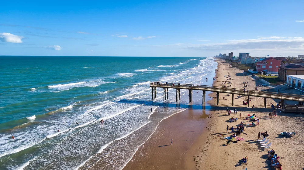 South Padre Island beach pier with tourists set up along the shore on a clear day to indicate one of the best spring break destinations for partying