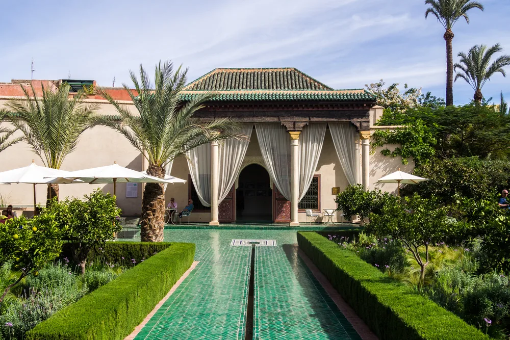 A luxurious riad at Le Jardin Secret in Marrakech, Morocco with palm trees and a pool outside the porch covered with curtains is an example of the top travel ideas for a bucket list trip