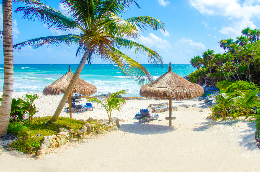 Tulum Beach on the Riviera Maya shown with thatched umbrellas and beach chairs, one of the best family vacations you can take in Mexico