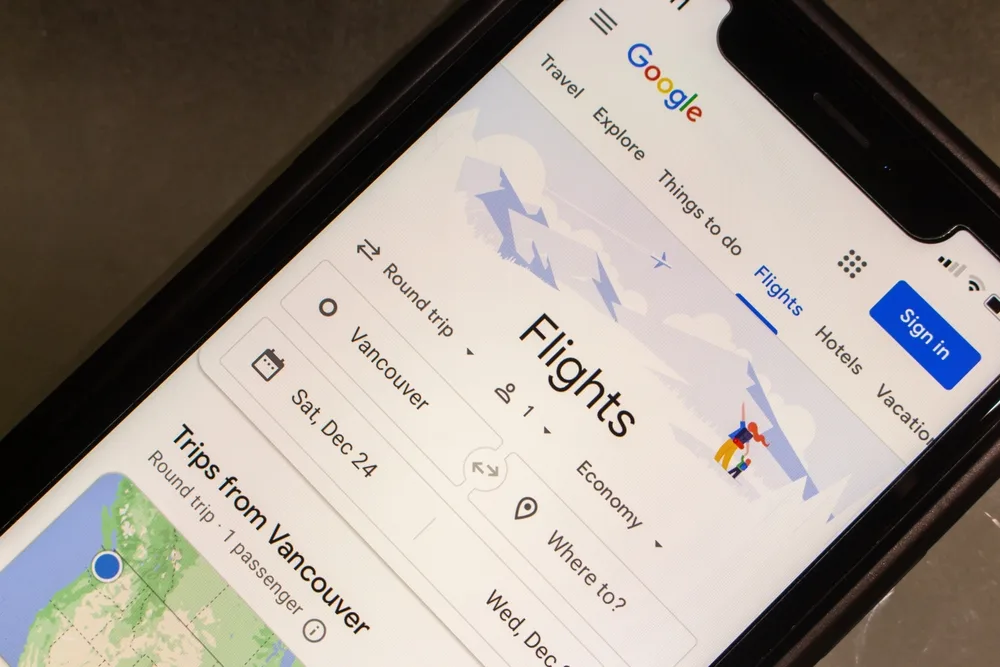 iPhone smartphone screen shown close-up with Google Flights open to show how to use Google Flights by entering the destination and departure details on the first search page