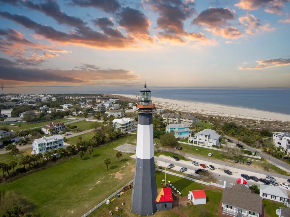 Tybee Island, GA shown from above with a lighthouse near the beach and homes nearby with clouds overhead as one of the best places to visit in the East Coast