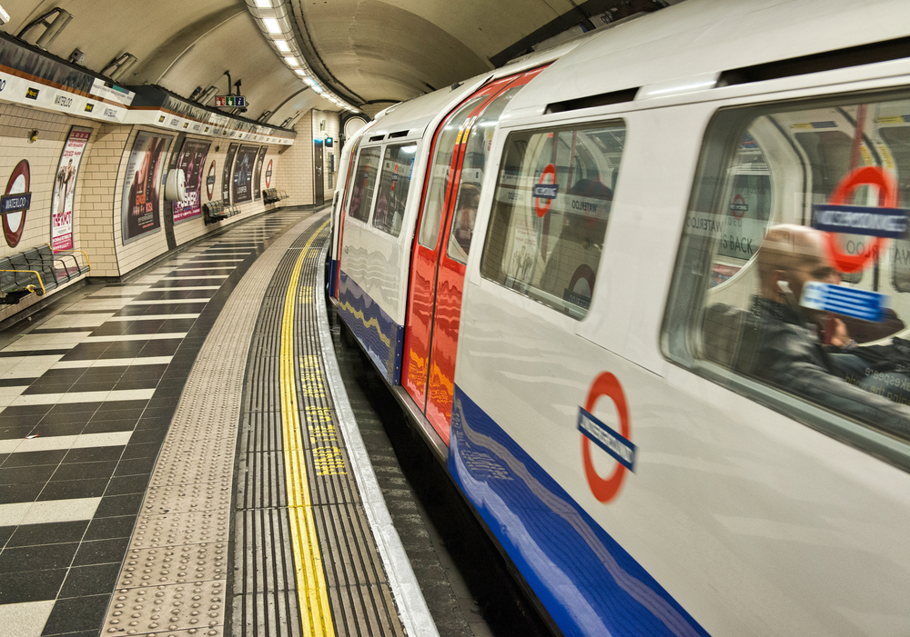 Photo of the London Tube train in white, red and blue color making its way by the photographer for a guide to the average London trip cost