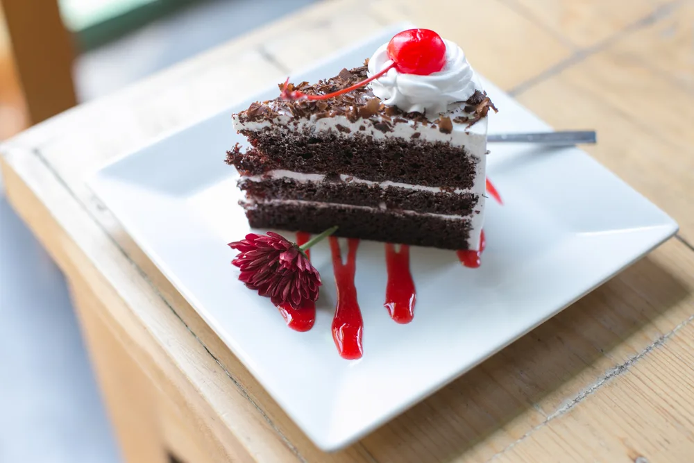 Black Forest cake slice topped with a cherry, whipped cream, chocolate shavings, and an edible flower indicate this could be the best German food to try among desserts