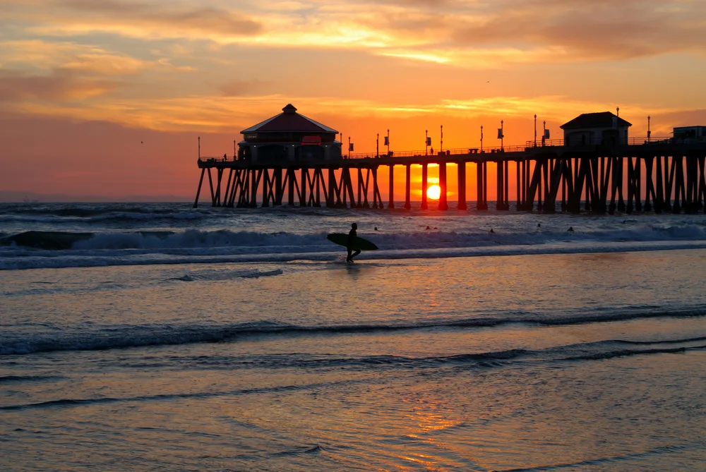 Silhouette of a surfer at sunset in front of the HB Pier on one of the best beach vacations from a list of the top 10 places