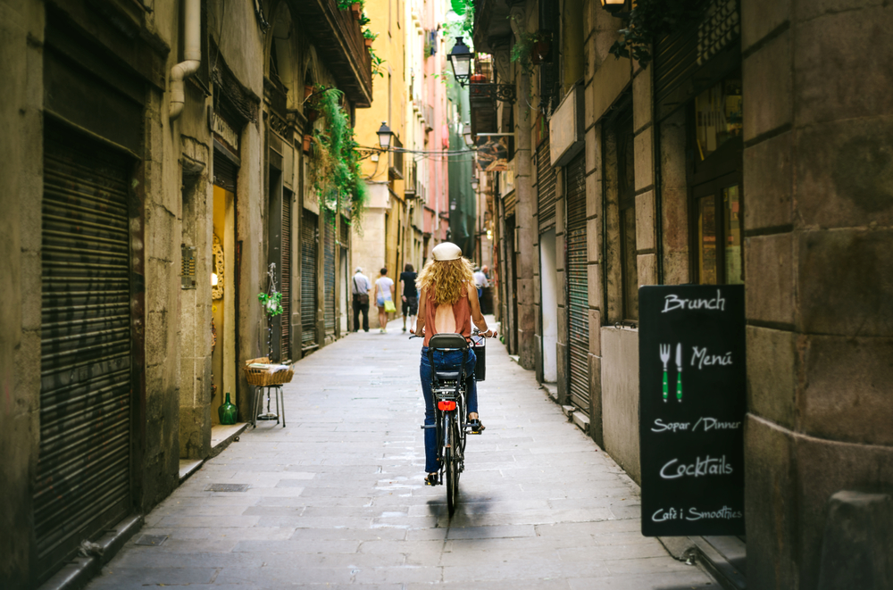 Woman in a white hat riding a bicycle through the middle of a cobblestone street in Barcelona