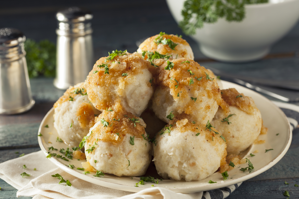 Plate full of German potato dumplings topped with gravy and chives shows one of the best German dishes you can try with salt and pepper shakers behind them