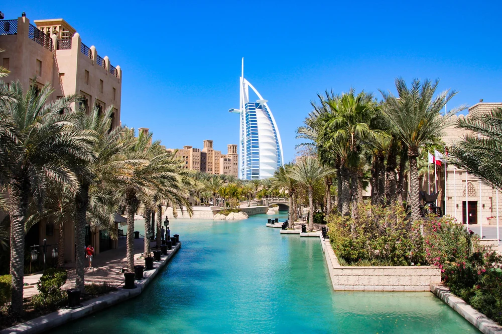 Burj al Arab seen from Madinat Jumeirah with its picturesque palm trees and canals for a guide titled Trip to Dubai Cost