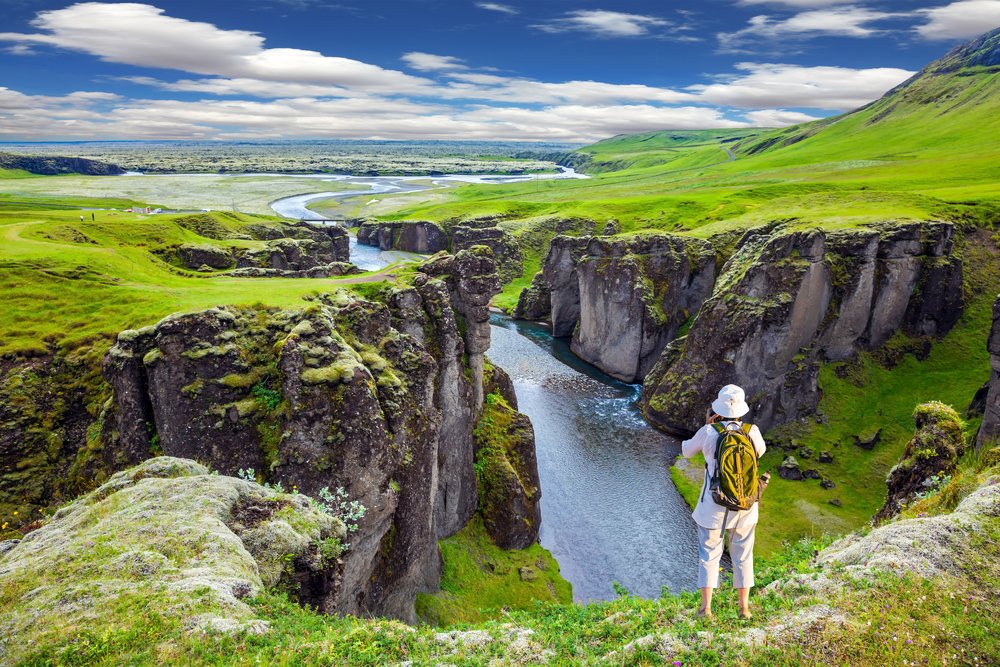 Woman in a neat white hat standing on the edge of a cliff overlooking the Fyadrarglyufur Canyon for an image for a piece on the average Icelandic trip cost