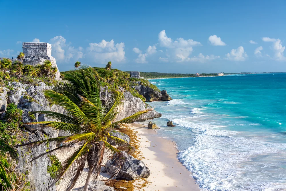 For a cost guide for a trip to Cancun, an aerial image of the ruins of Tulum pictured overlooking the teal water and white-sand beach in Tulum