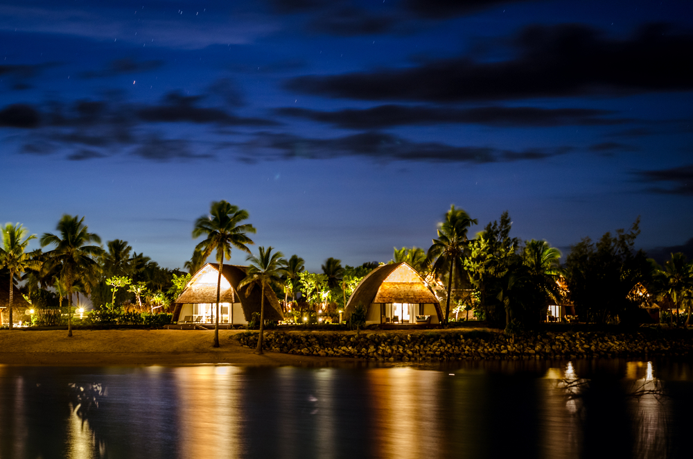 Black night with Fijian huts illuminating the rocky and sandy shoreline below