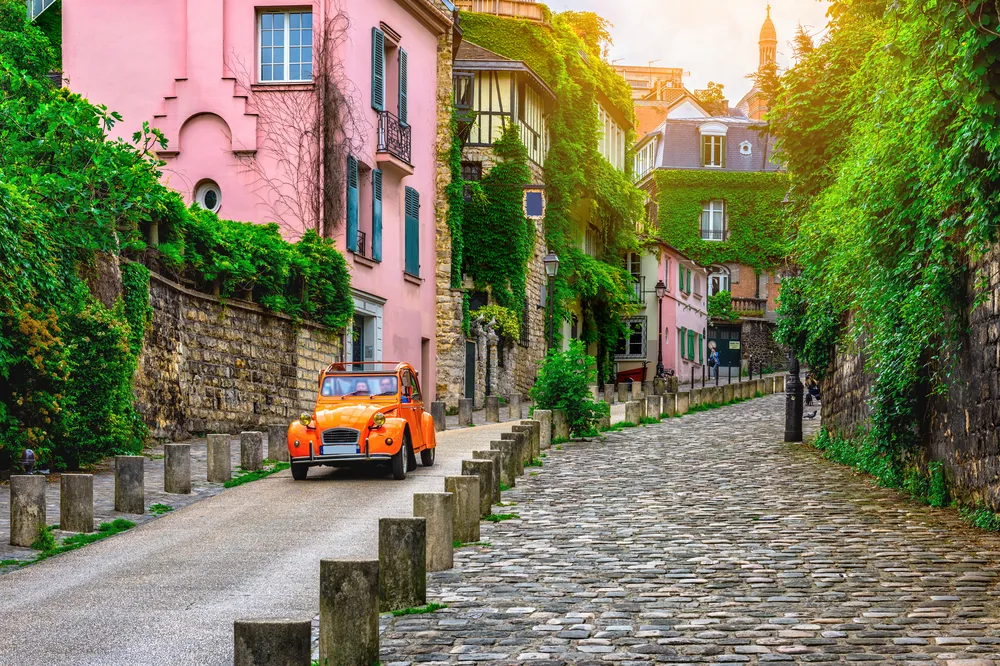 View of an orange car driving down the paved street in Montmartre for a guide to whether or not Paris is safe to visit