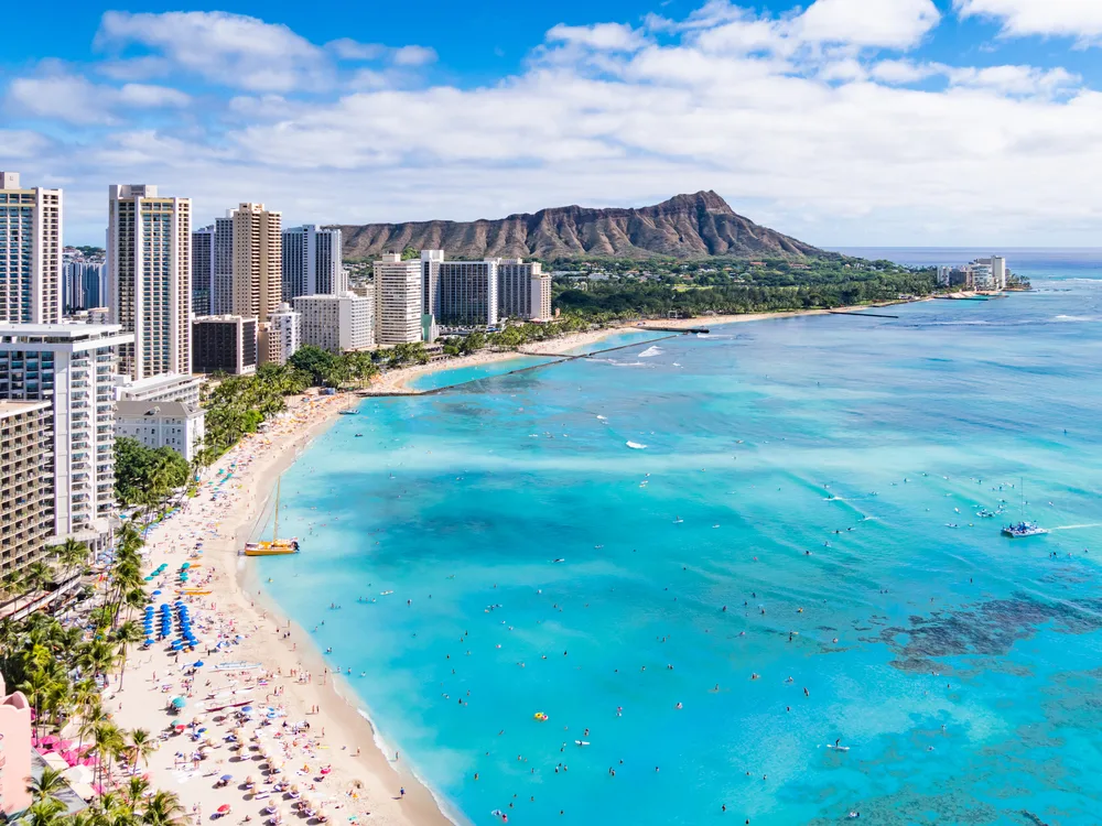 Aerial view of Honolulu's Waikiki Beach and Diamond Head crater with people on the shore to show one of the best family vacations for all ages