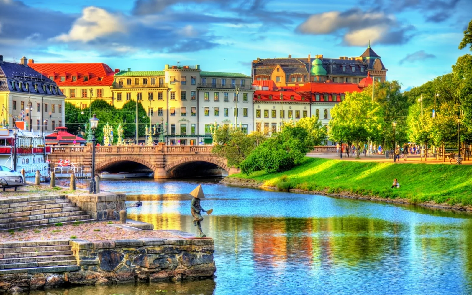 Old structures along a river, and people walking on the riverbank during a sunset, a pick for the featured image on an a travel guide about trip to Sweden cost.