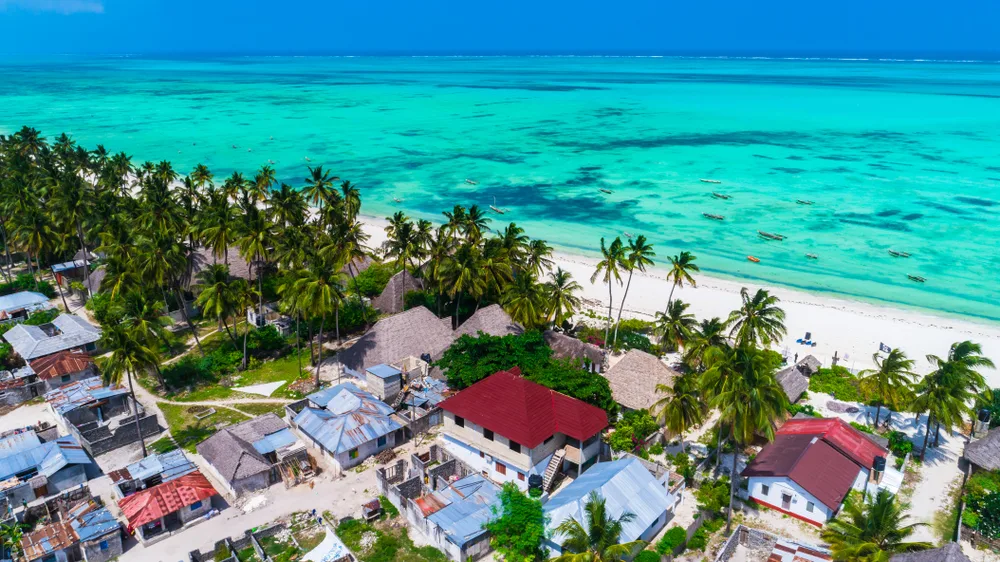 Aerial view of a town in Jambiani, one of the best places to stay in Zanzibar, with residential structures near the emerald beach with coconut trees. 