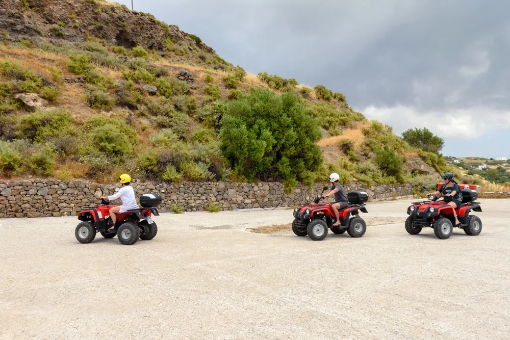 Three people riding red ATVs while wearing helmets on a rough road. 