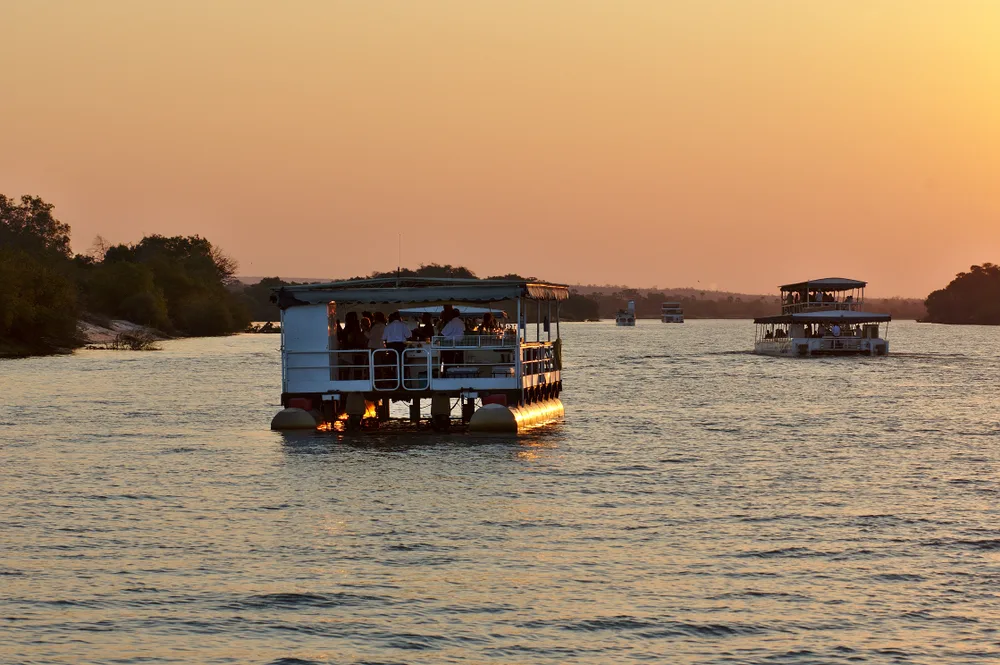 Two large native tourist ships crossing a wide river during sunset. 