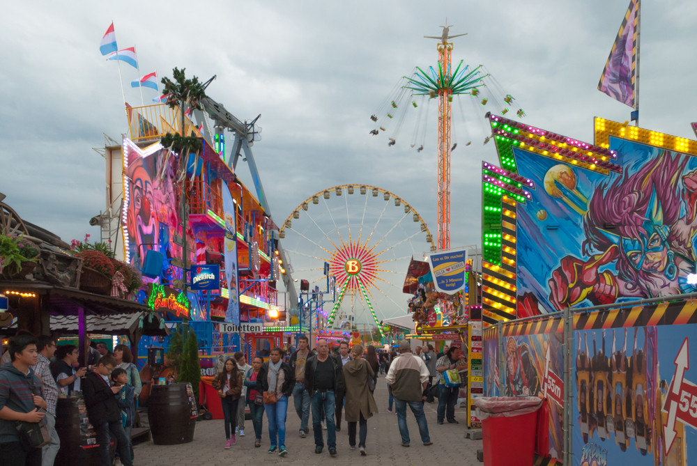 Photo of the Schueberfouer fair with its neon-lit rides and people among them on a cloudy day
