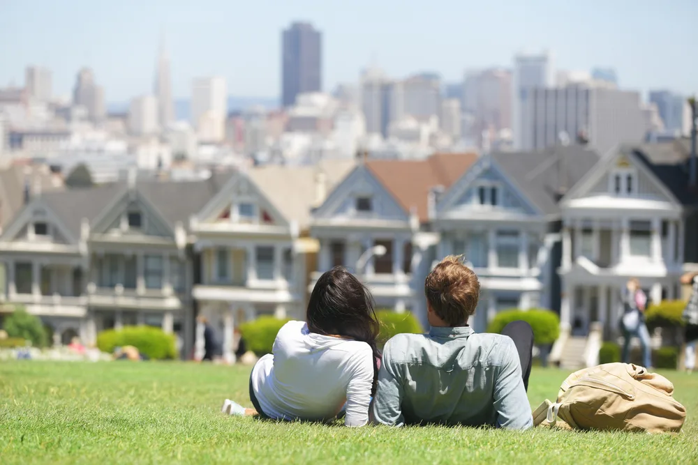 A couple laying in the grass while observing the city from a distance. 