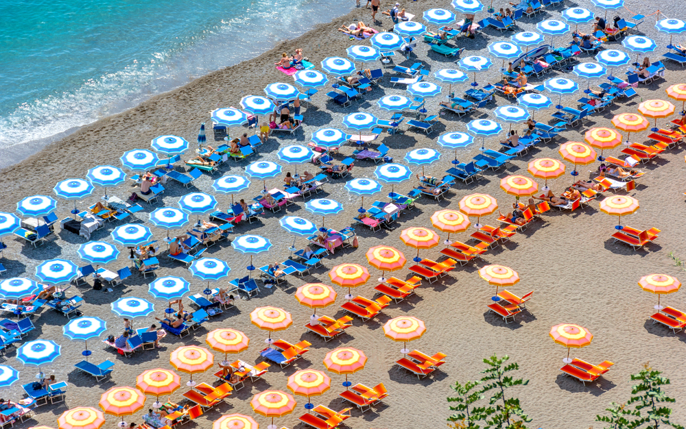Large umbrellas covering people on the sun beds on a calm beach.