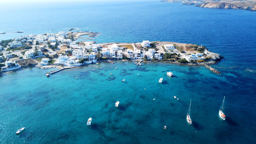 Small boats can be seen anchored distant font the pier, where a coastal town can be seen with white structures. 