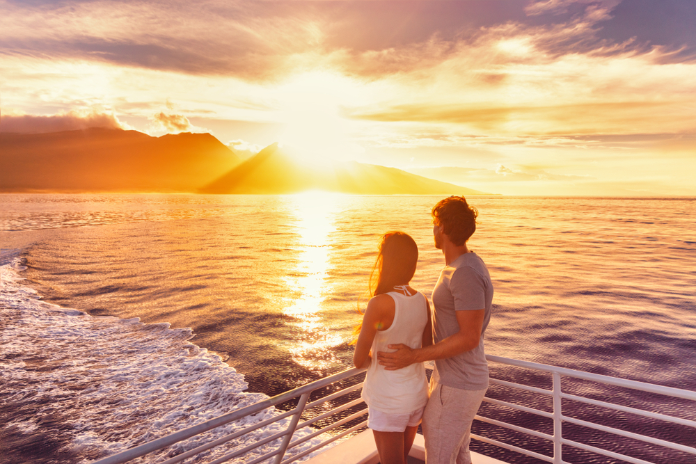 A sweet couple standing on the edge of a boat while looking at the sunset. 