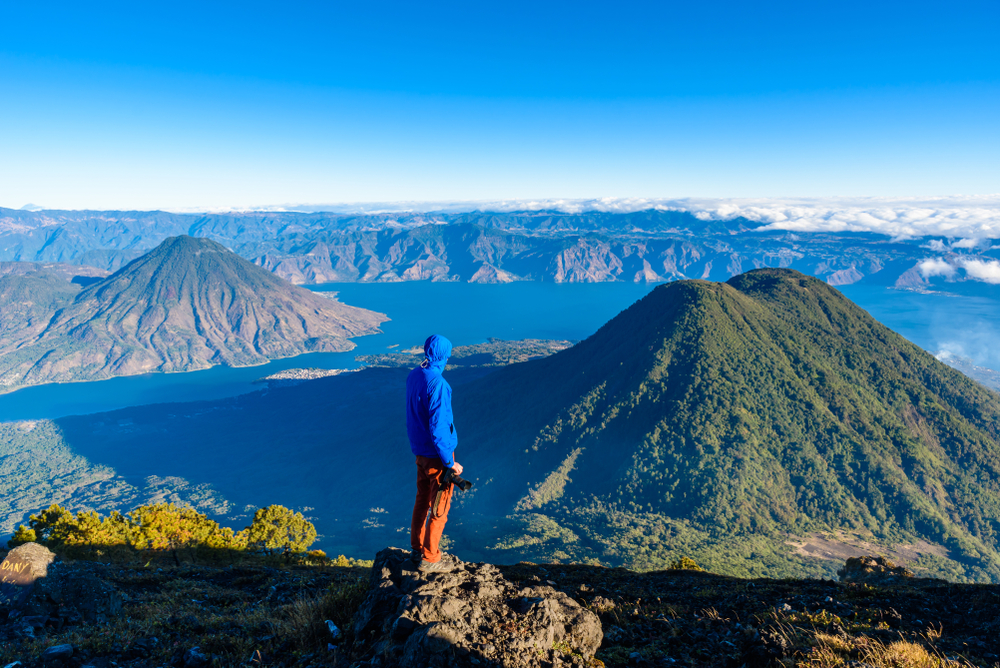 Hiker standing atop the Lake Atitlan mountain and the San Pedro volcano wearing a blue coat