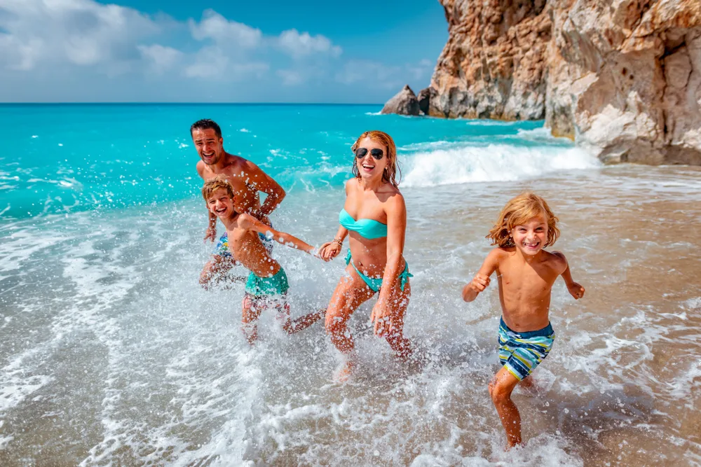 A family of four can be seen enjoying running at a beach while wearing swimming wears during a summer.