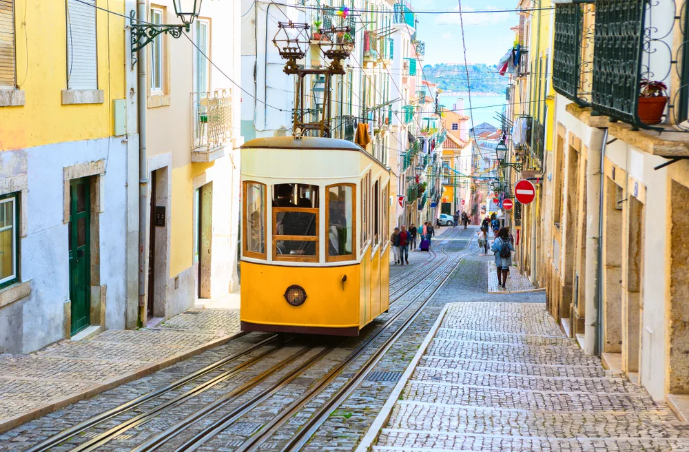 View of the yellow tram making its way up the cobblestone street between buildings for a guide titled Is Lisbon Safe to Visit