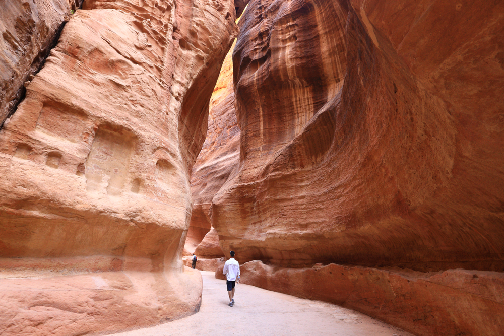 A man passing through a canyon of orange rocks. 
