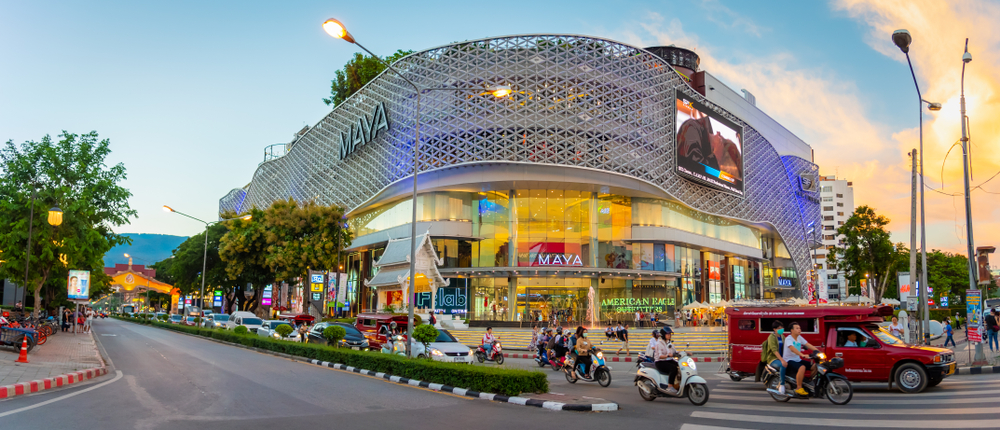 A wide view of a street in front of a mall where cars and motorcycles are sharing the road. 