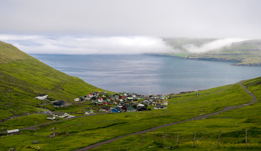 A small village consists of very few houses has grass-covered fields facing a very calm sea. 