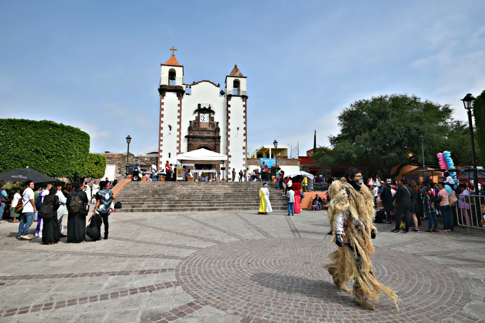 A local man wearing traditional clothing passing a the front of a church in San Antonio, a top pick for the best places to stay in San Miguel, while tourists are busy scanning the place. 