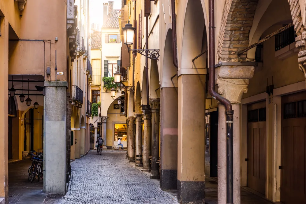 A narrow alley with brick street in between large building columns, an image for a travel guide about safety in visiting Milan.
