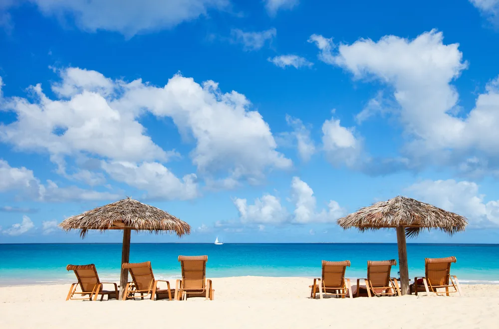 Three sun beds placed below each of the two native umbrella-shaped shade on the a beach with white fine sand and emerald water.