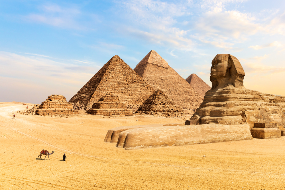 The ever famous pyramid and sphinx in the Egyptian desert of Giza, one of the best areas to stay in Cairo, and a man with his camel can be seen walking towards the structure.