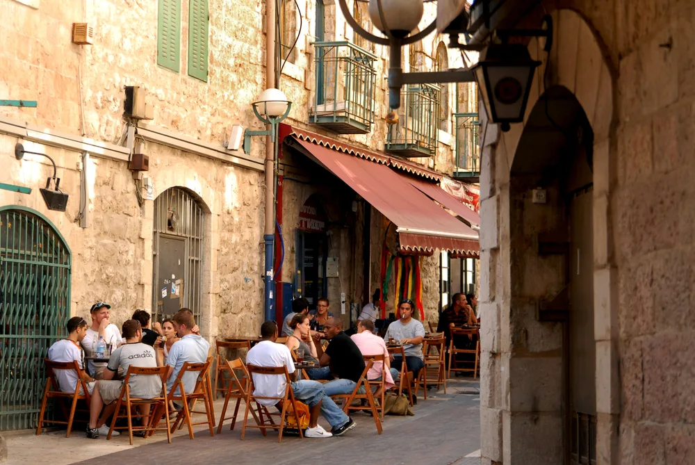 People can be seen eating on an outdoor dining of a restaurant in a small alley. 