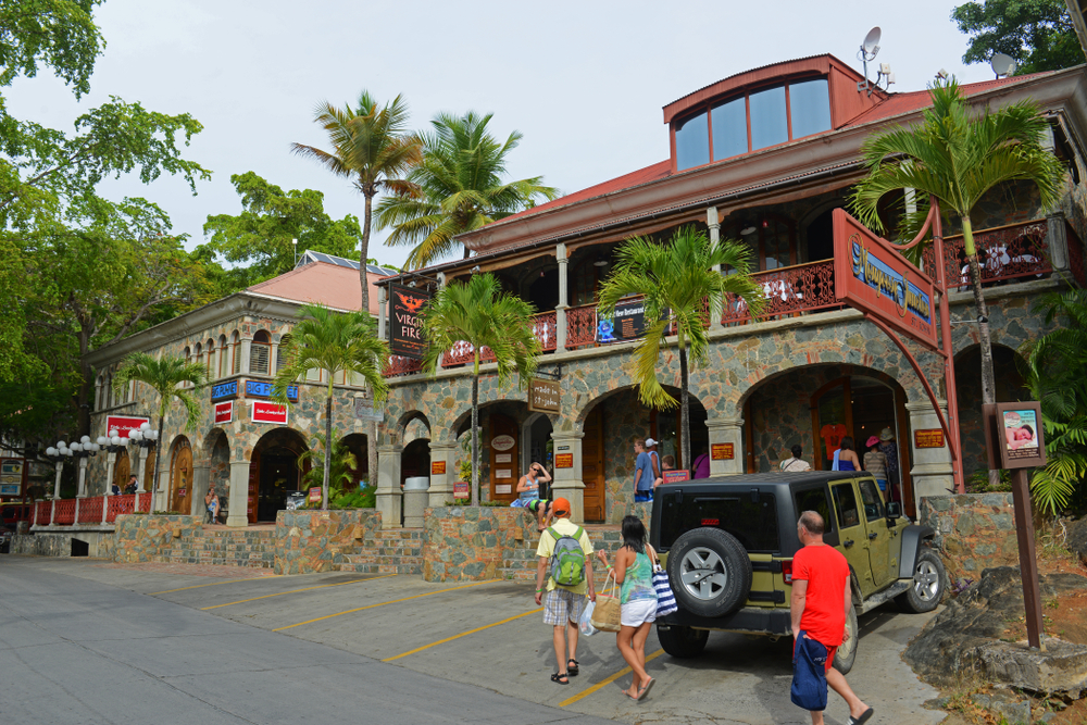 Tourists can be seen walking on a road beside a two-story structure with a parked jeep. 