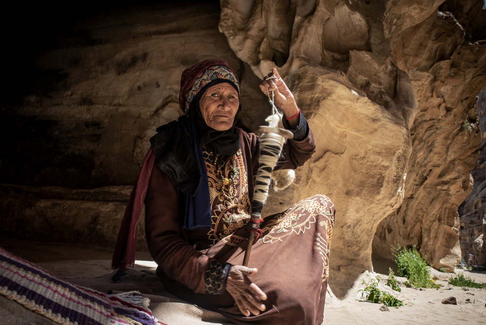 A local old woman sitting on the rock while taking shade, holding her walking stick. 