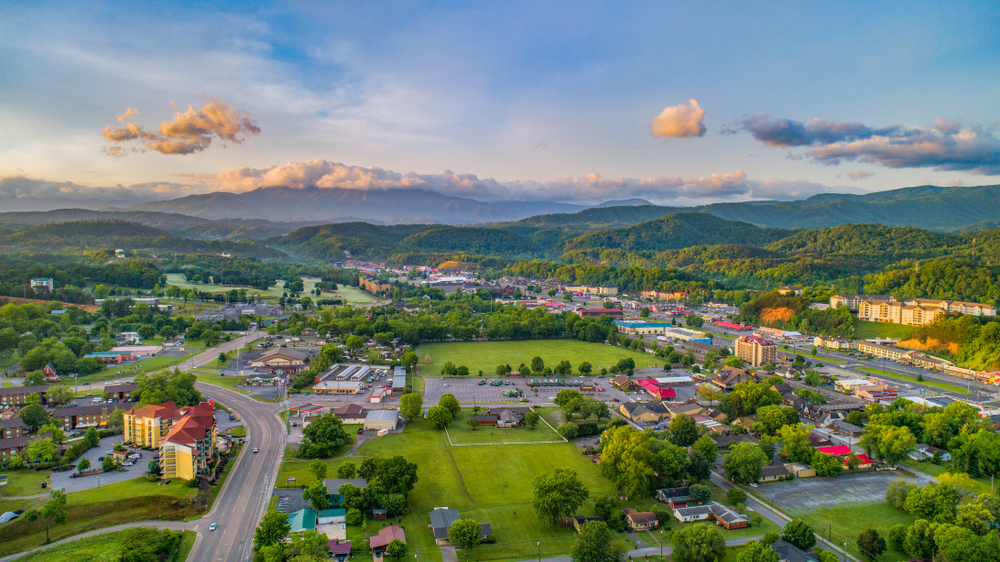 Aerial view on a small town with few structures and large area of green fields and forest, captured for a piece on an article about trip cost to Pigeon Forge. 