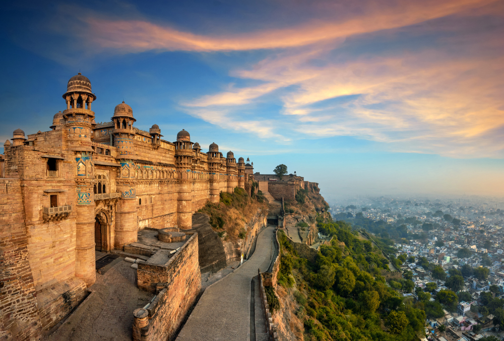 Gwalior Fort in India pictured for a guide to the average cost of a vacation to India with its gorgeous view overlooking the city below and a peach sky above