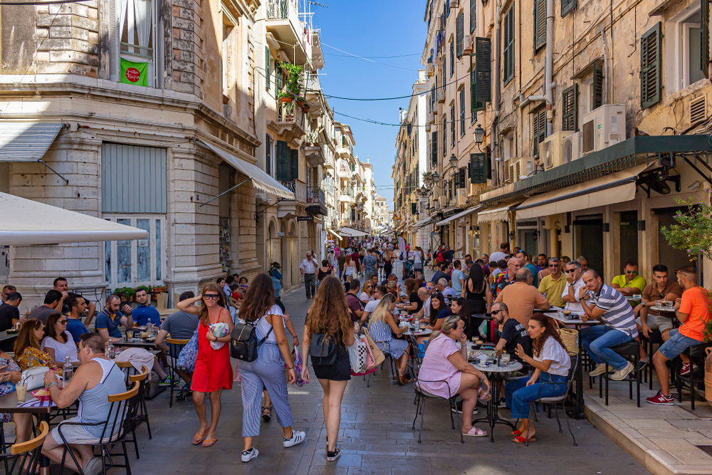 A busy street where people are seen eating in restaurants and others are seen walking. 