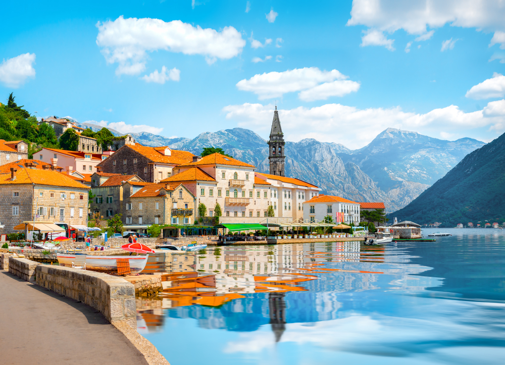 Perast, Montenegro at Bay of Kotor on a beautiful day with buildings reflecting on the water for a list of the cheapest places to travel in Europe