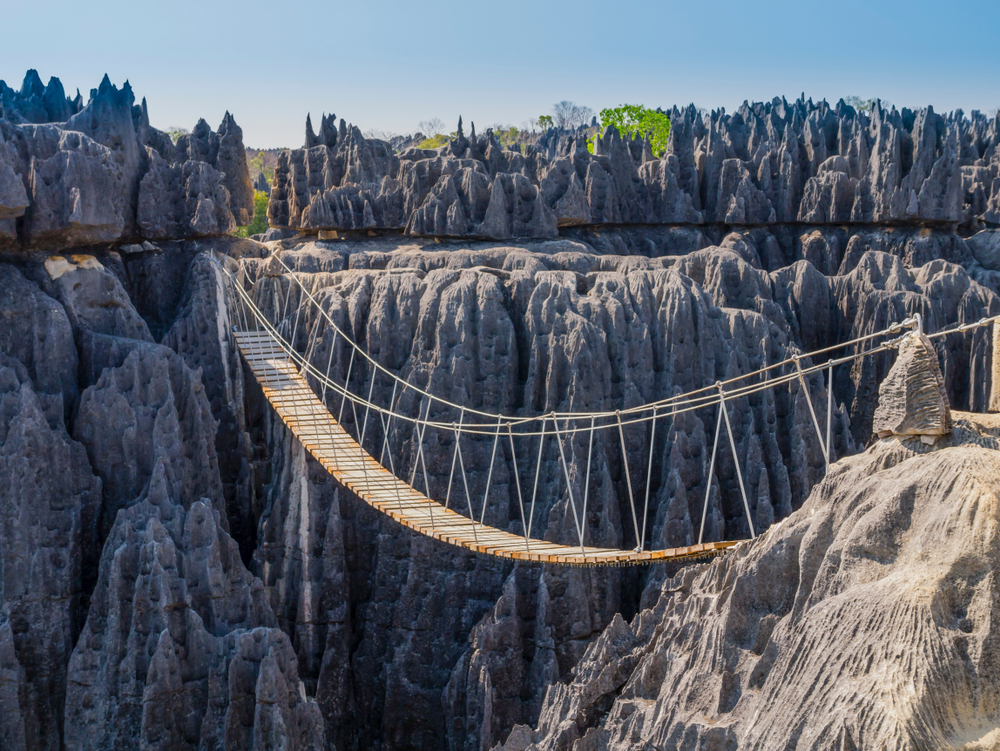 A wooden hanging footbridge crossing a gap of a canyon with pointy rocks. 