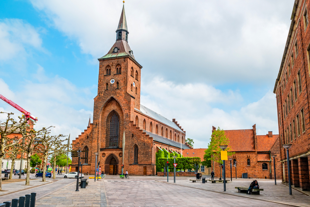 A historic church made of bricks fronting an empty square with a few cars seen passing by. 