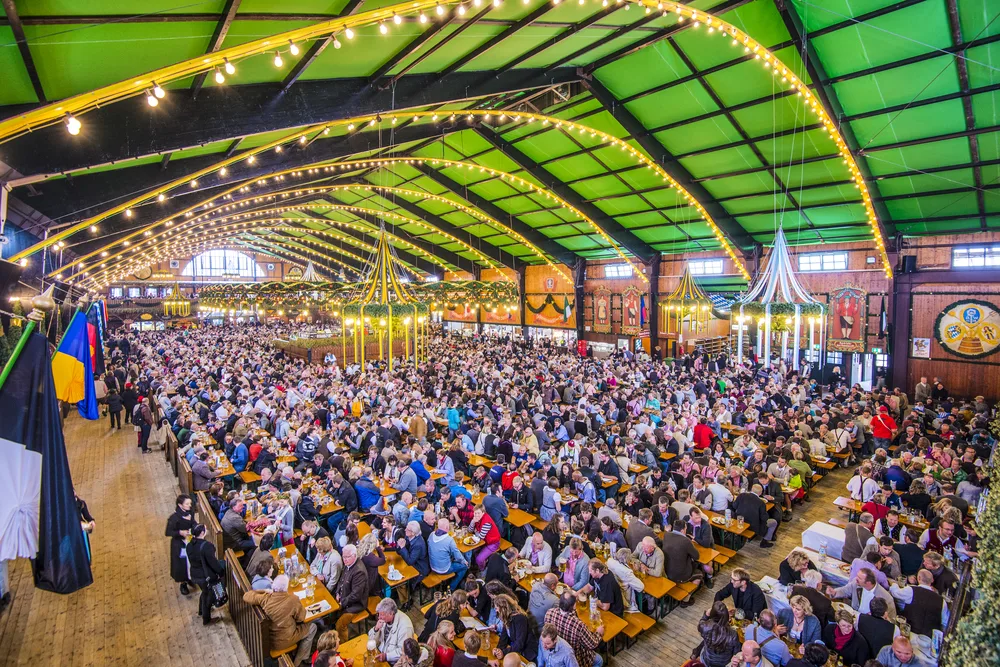 A large crowd sitting on chairs and tables inside a large tent while eating and drinking. 