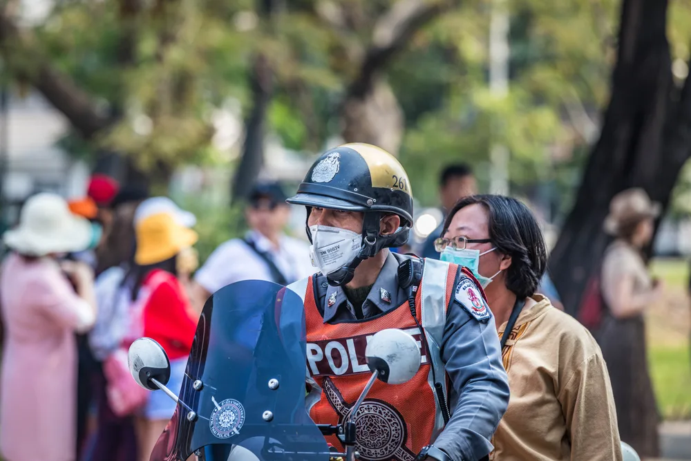 A police riding his motorcycle with a civilian personnel, both of them are wearing face masks. 