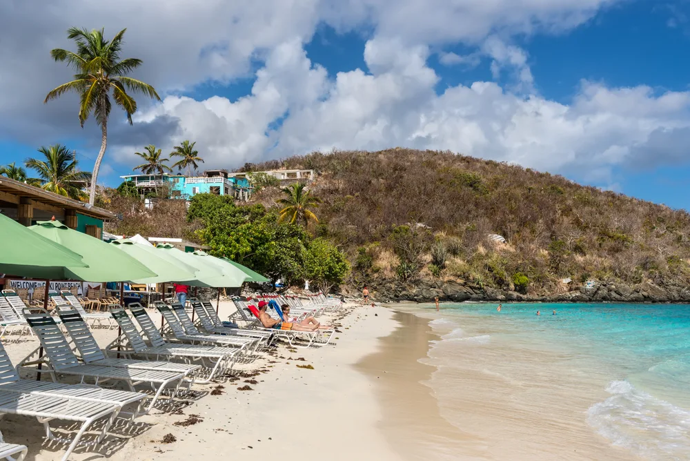 To help answer the question Is St. Thomas Safe to Visit, a photo of the Coki Point Beach pictured on a nice day with its old beach chairs next to the beige sand