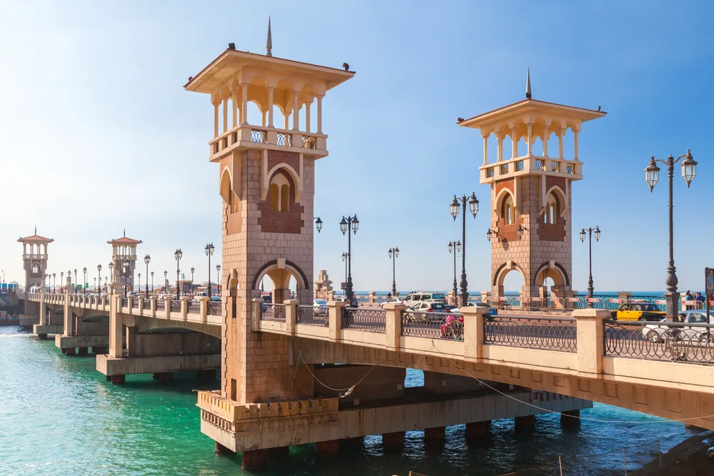 A bridge that has two watch towers on both ends in Alexandria, one of the best areas to stay in Egypt, cars passing by the bridge during a hot afternoon.
