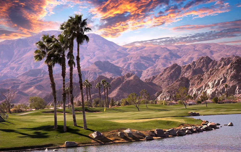 A golf course in Palm Springs, California at sunset with clouds overhead and tall palm trees in front of the mountains for a Northern vs Southern California climate comparison